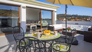 Une terrasse sur le toit équipée d’une table à manger, de chaises, d’un grand parasol et d’un canapé.