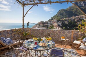 A terrace with a tiled table set for dining, overlooking a coastal town. - Palazzo Crocione in Positano (Positano)