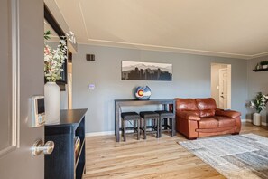 A modern living room with a brown leather sofa, a wooden coffee table, and a cityscape painting.