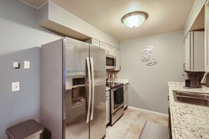 A compact kitchen with a stainless steel refrigerator, microwave, oven, and a granite countertop.