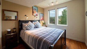 Un dormitorio con una cama, lámparas de noche, una mesita de noche, un espejo y dos ventanas con vistas a zonas verdes.