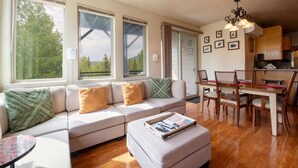 Una sala de estar amplia con un sofá grande, una zona de comedor con sillas de madera y una cocina al fondo.