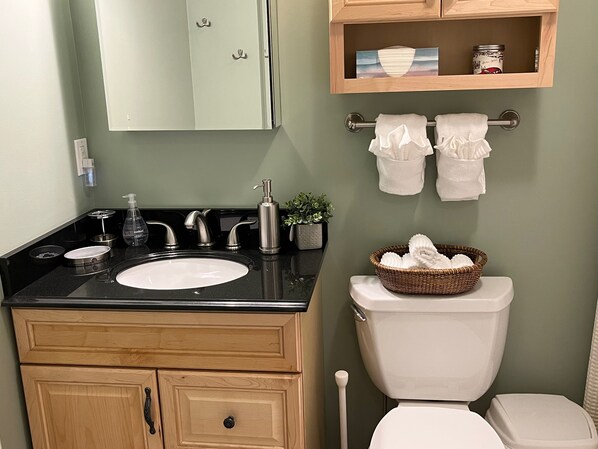 A bathroom with a sink, two faucets, a toilet, a mirror, and a shelf with towels and a basket. - Upgraded Family-sized Mountain View Condo with Loft! (Lincoln)