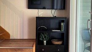 Una sala de estar con un televisor de pantalla plana montado en la pared, una escalera de madera, un mueble de entretenimiento negro con estantes, una planta en maceta y una cesta de mimbre.
