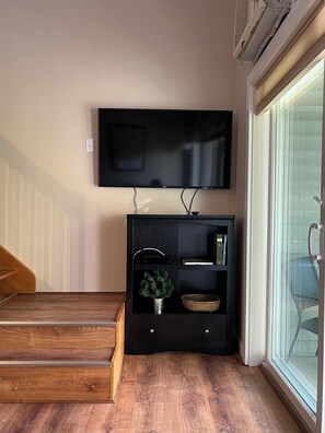 A living room with a flat-screen TV mounted on the wall, a wooden staircase, a black entertainment unit with shelves, a potted plant, and a wicker basket. - Upgraded Family-sized Mountain View Condo with Loft!   (Lincoln)