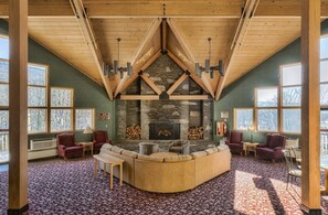 A cozy living room with a stone fireplace, wooden ceiling beams, and large windows. - Upgraded Family-sized Mountain View Condo with Loft! (Lincoln)