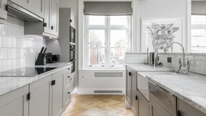 A modern kitchen with grey cabinets, a herringbone wood floor, and a large window with a view of the city. - The Connaught Suite in London (London)