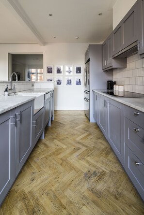 A modern kitchen with grey cabinets, a wooden herringbone floor, and a large island with a sink.