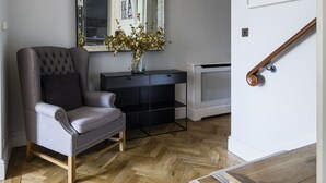 A room with a tufted armchair, a vanity with a mirror, and a herringbone wooden floor.