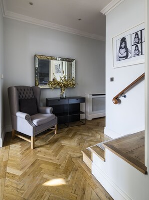 A room with a tufted armchair, a vanity with a mirror, and a herringbone wooden floor. - The Connaught Suite in London (London)