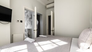 A bedroom with a bed, a TV mounted on the wall, and a bathroom visible through an open door.
