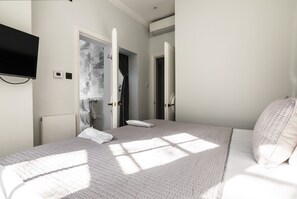 A bedroom with a bed, a TV mounted on the wall, and a bathroom visible through an open door. - The Connaught Suite in London (London)