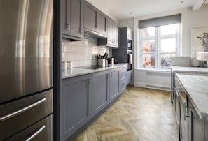 A modern kitchen with grey cabinets, stainless steel appliances, and a herringbone wood floor. - The Connaught Suite in London (London)