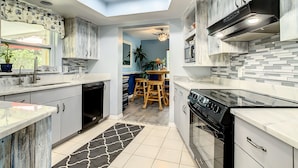 A modern kitchen with white cabinets, a black stove, and a tiled backsplash. - Private Beach House Paradise (Melbourne Beach)