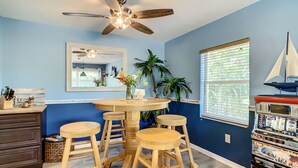 A kitchen with a round table, wooden stools, a ceiling fan, a window with blinds, and a jukebox. - Private Beach House Paradise (Melbourne Beach)