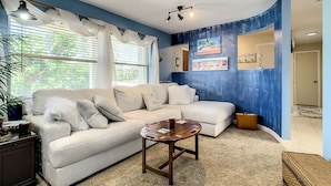 A living room with a white sectional sofa, a wooden coffee table, and a blue accent wall. - Private Beach House Paradise (Melbourne Beach)