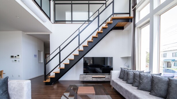 A modern living room with a glass coffee table, a sofa with cushions, a staircase, and a television. - THE BEEHIVE KAMIFURANO (Kamifurano)