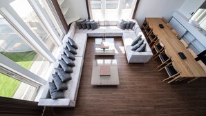 A modern living room with a sectional sofa, a wooden dining table, and a glass coffee table. - THE BEEHIVE KAMIFURANO (Kamifurano)