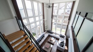 A spacious room with a large window, a wooden staircase, and a modern sofa set. - THE BEEHIVE KAMIFURANO (Kamifurano)