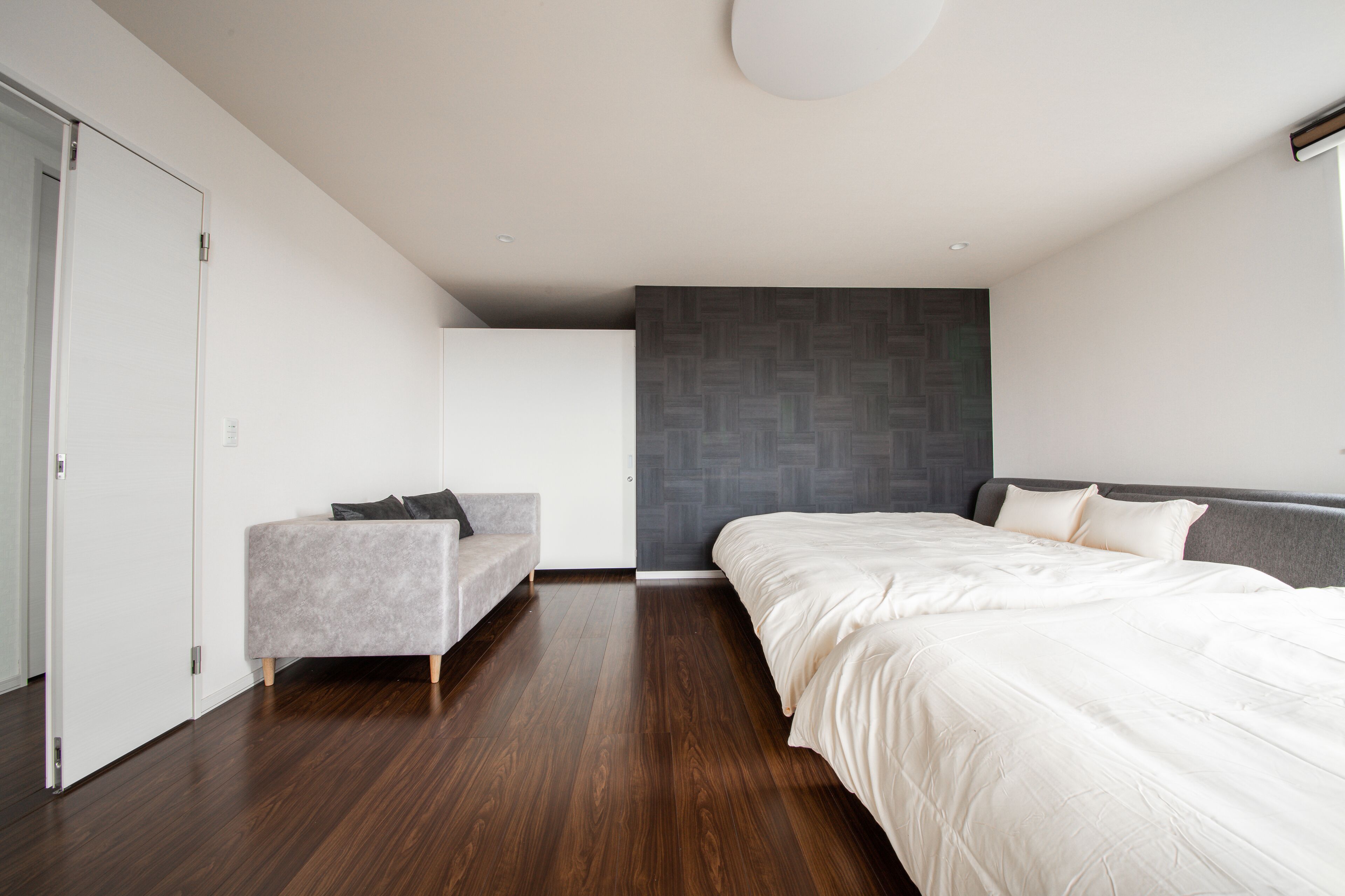 Ein modernes Schlafzimmer mit einem großen Bett, einem grauen Sofa und einem Kleiderschrank.