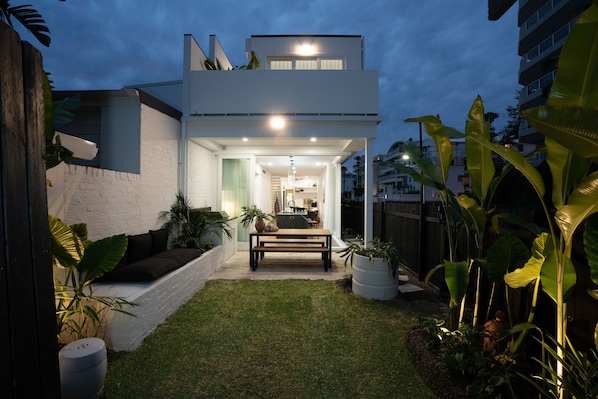 Een modern huis met een verzorgd gazon, een terras met een bankje, en grote potplanten.