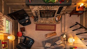 Ein gemütliches Wohnzimmer mit Kamin aus Stein, einem Fernseher, einem Ledersessel, einer Couch und dekorativen Lampen.