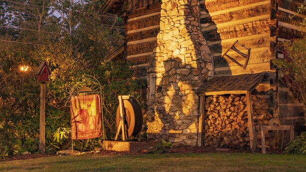 Ein rustikales Holzhaus mit einem Steinkamin, umgeben von Bäumen und einem gepflegten Rasen.