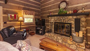Ein gemütliches Blockhaus-Interieur mit Kamin aus Stein, Ledersofa und Fernseher.