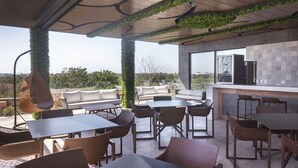 An outdoor patio with a variety of seating options, including tables and chairs, and a bar area with a tiled backsplash. - Menesse PH (Tulum)