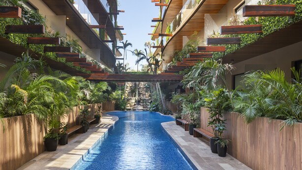 A pool area with a clear blue pool, wooden benches, and lush greenery. - Menesse PH (Tulum)