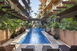 Zona de piscina con una piscina azul cristalina, bancos de madera y abundante vegetación.
