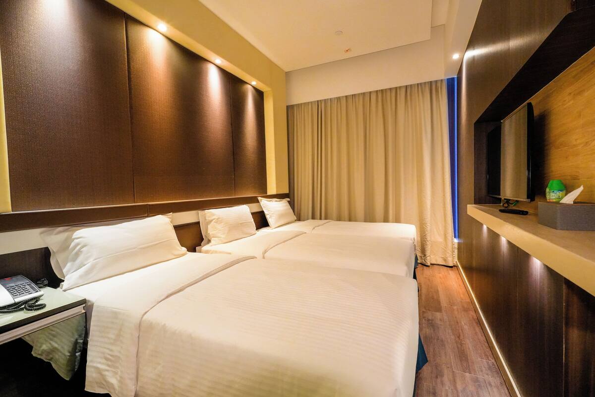 A hotel room with two beds, a desk with a laptop, a telephone, and a television on a wooden panel.