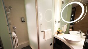 A modern bathroom with a glass shower enclosure, a white sink, and a large mirror with a circular frame. - Epoch Hotel (Kowloon)
