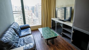 A living room with a leather sofa, a coffee table with a board game, a flat-screen TV, and a view of a cityscape through large windows. - Epoch Hotel (Kowloon)