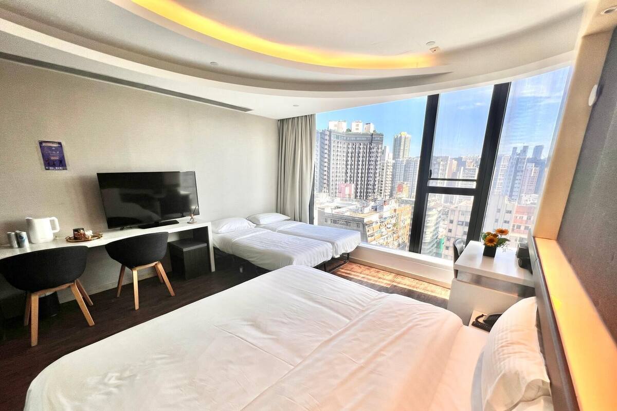 A hotel room with a large bed, a desk with a TV, and a view of the city.