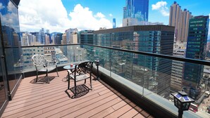 A high-rise balcony with a city view, furnished with two chairs and a table, and a glass railing. - Epoch Hotel (Kowloon)