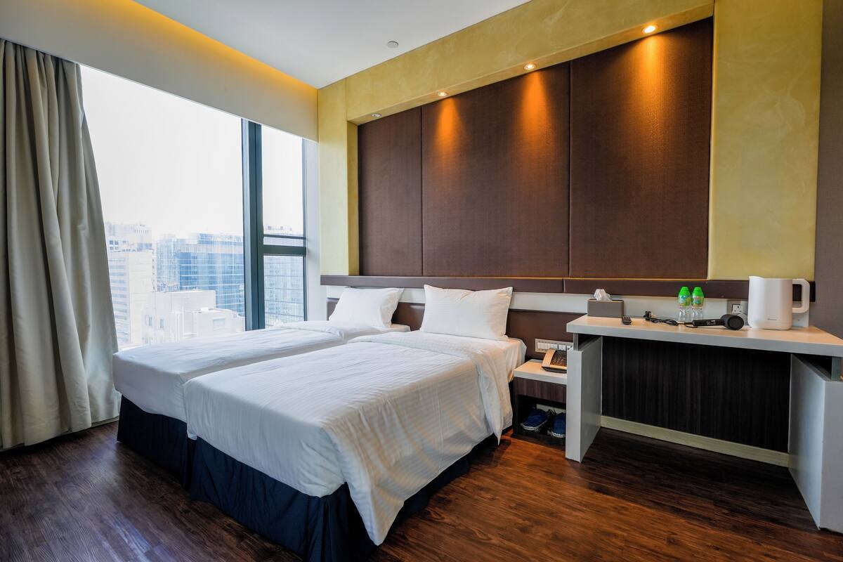 A hotel room with two beds, a desk with a coffee maker, and a view of the city.