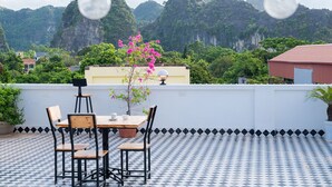 Una terrazza sul tetto con pavimento a scacchi, un tavolo con sedie e una pianta in vaso con fiori rosa.