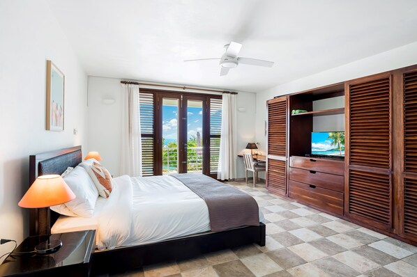 A bedroom with a bed, bedside lamp, ceiling fan, and a TV on a wooden cabinet.