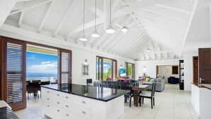 Een ruime keuken met een groot eiland, witte kasten en een hoge plafond met zichtbare balken.