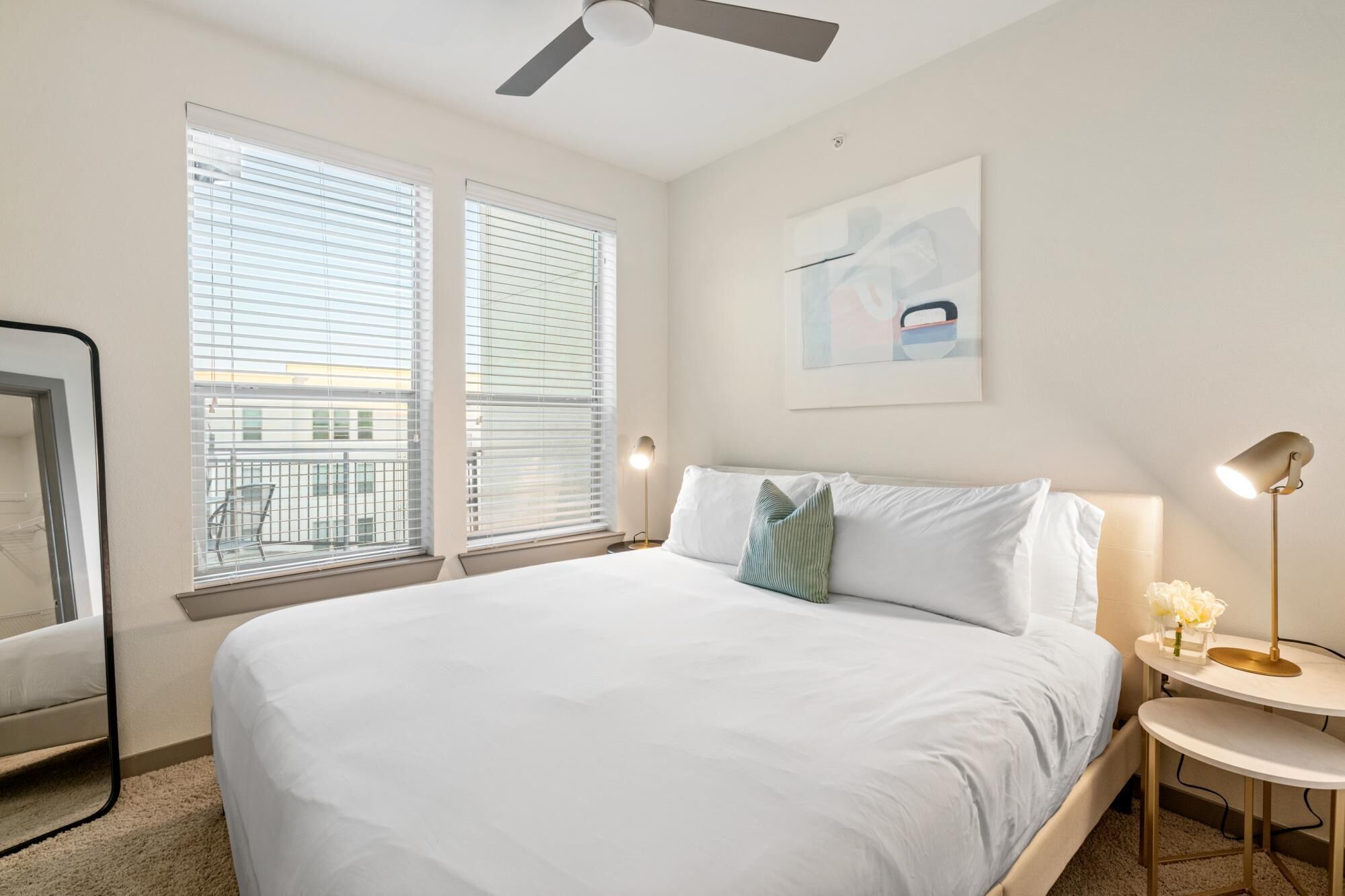 A hotel room with a large bed, two bedside tables, a ceiling fan, and a window with blinds.