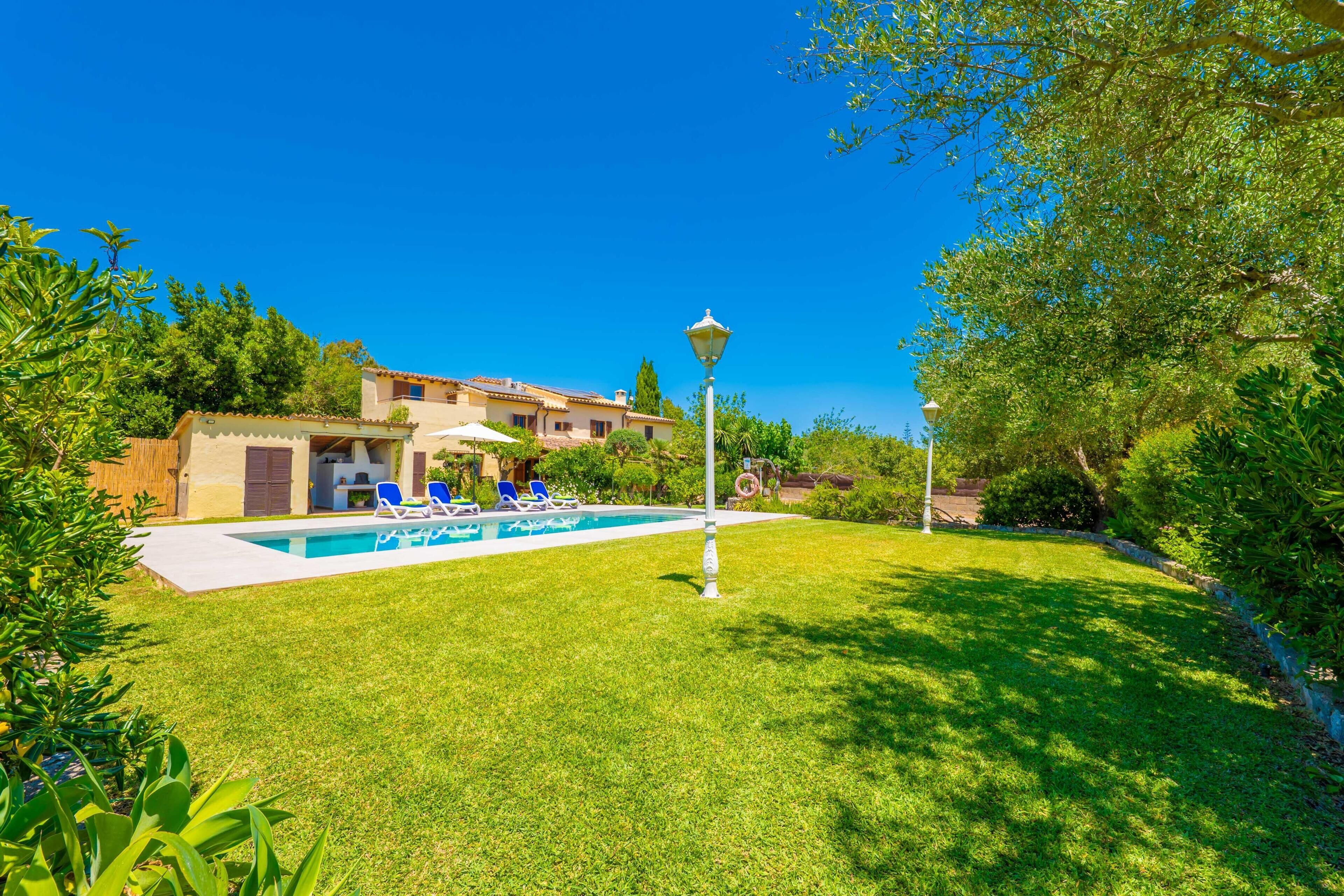 A swimming pool with lounge chairs, a lamp post, and a building with a tiled roof in the background.