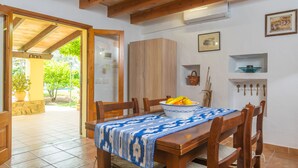 A dining area with a wooden table, chairs, and a bowl of fruit. There is a wooden cabinet and a wall-mounted shelf with a bowl. - MARINA (POLLENÇA)  - Charming country house with private swimming pool and free WiFi (Pollença)