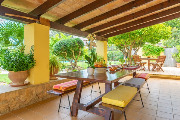 Un patio al aire libre con una mesa de madera, bancos y plantas en macetas.