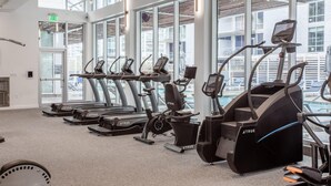 A gym with multiple exercise machines, large windows, and a view of a pool area. - Austin Beautiful 1BD 1BA 2nd Street District Apartment (Austin)