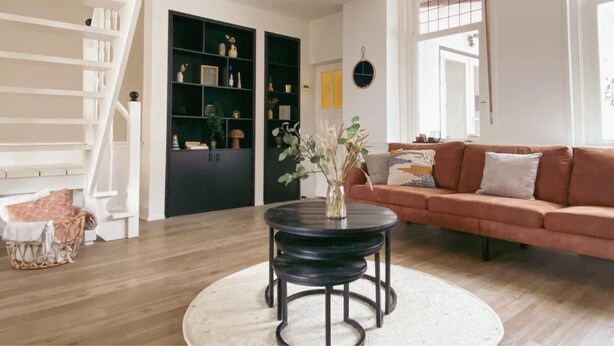 Una sala de estar con una mesa redonda, un sofá, una estantería y una escalera.