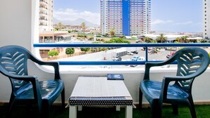A balcony with two chairs and a table, overlooking a cityscape with high-rise buildings and a parking area.
