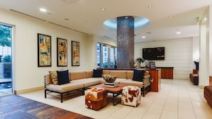 A spacious living area with a sectional sofa, two ottomans, a coffee table, and a fireplace. There are framed artworks on the wall and a flat-screen TV mounted above the fireplace. - Austin Beautiful Studio Apartment (Austin)