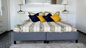 Ein Doppelbett mit gemustertem Bettbezug, zwei Nachttischlampen und ein Spiegel über dem Bett.