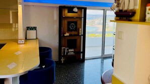 Ein Zimmer mit einem runden Tisch, blauen Stühlen, einer Bücherwand mit nautischen Dekorationen und Meerblick durch ein großes Fenster.